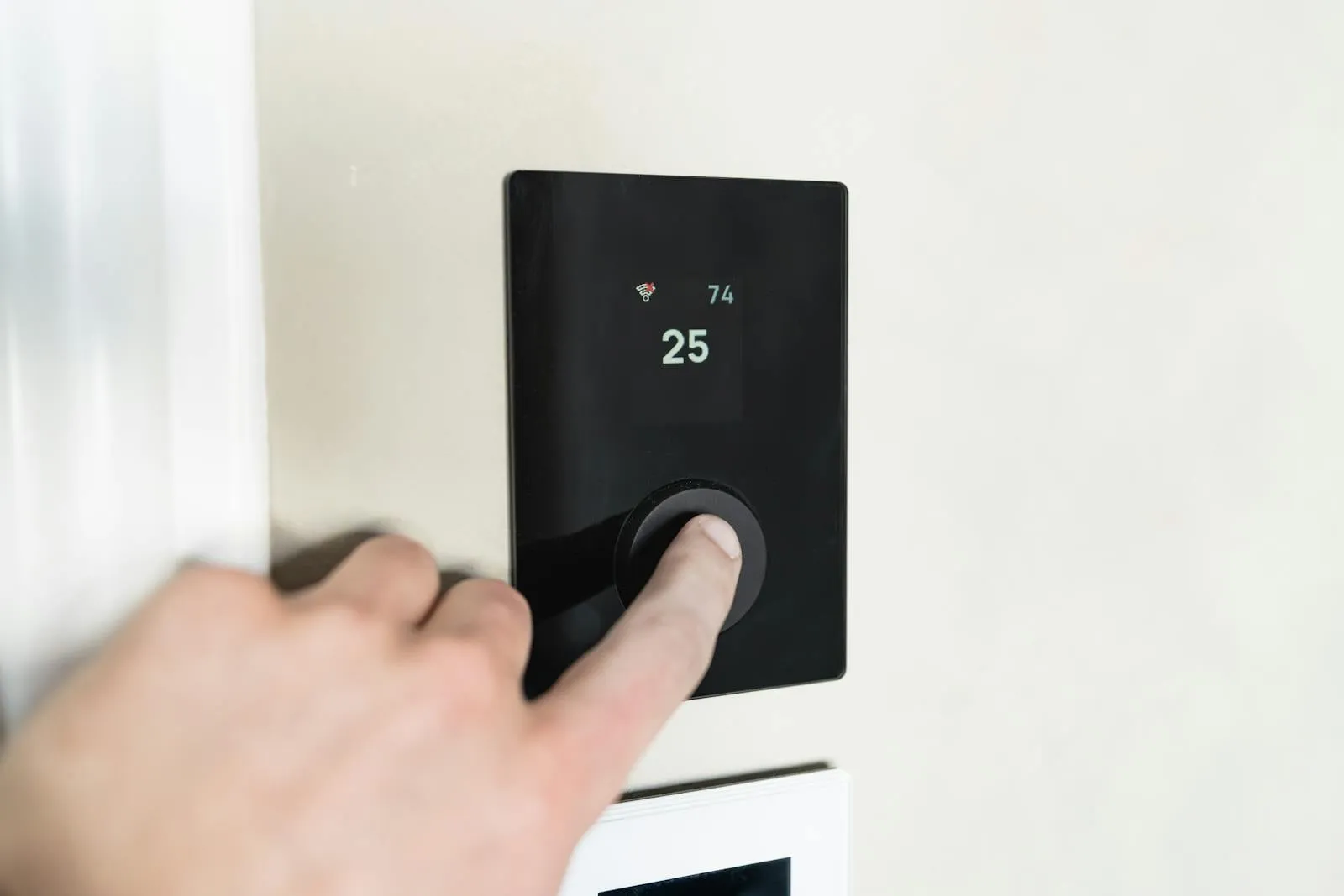 A hand adjusting a smart thermostat — steady, low-temperature running is what turns a heat pump's efficiency into savings that pay it back.